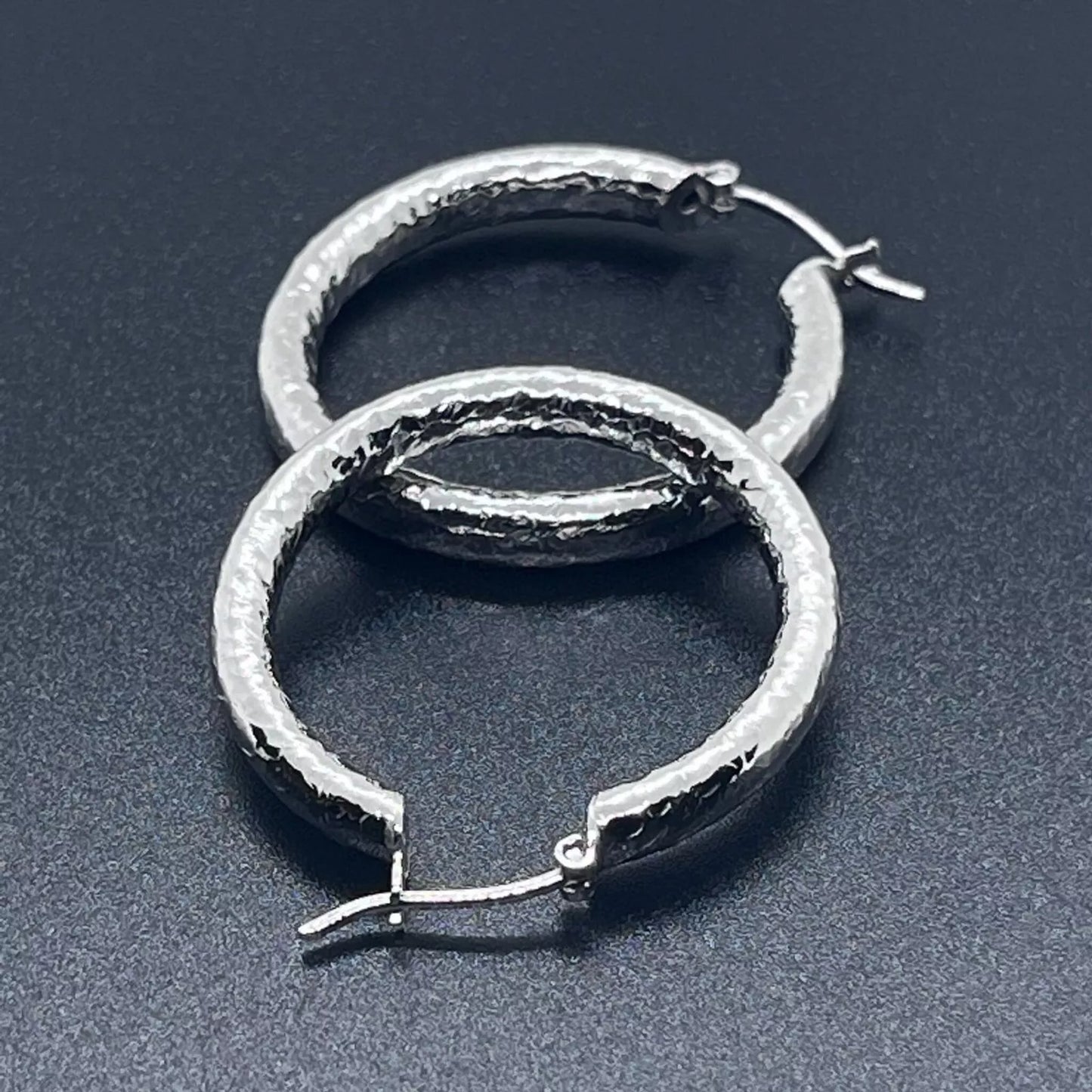 Silver creole hoop earrings crafted in 925 sterling silver on a back background.