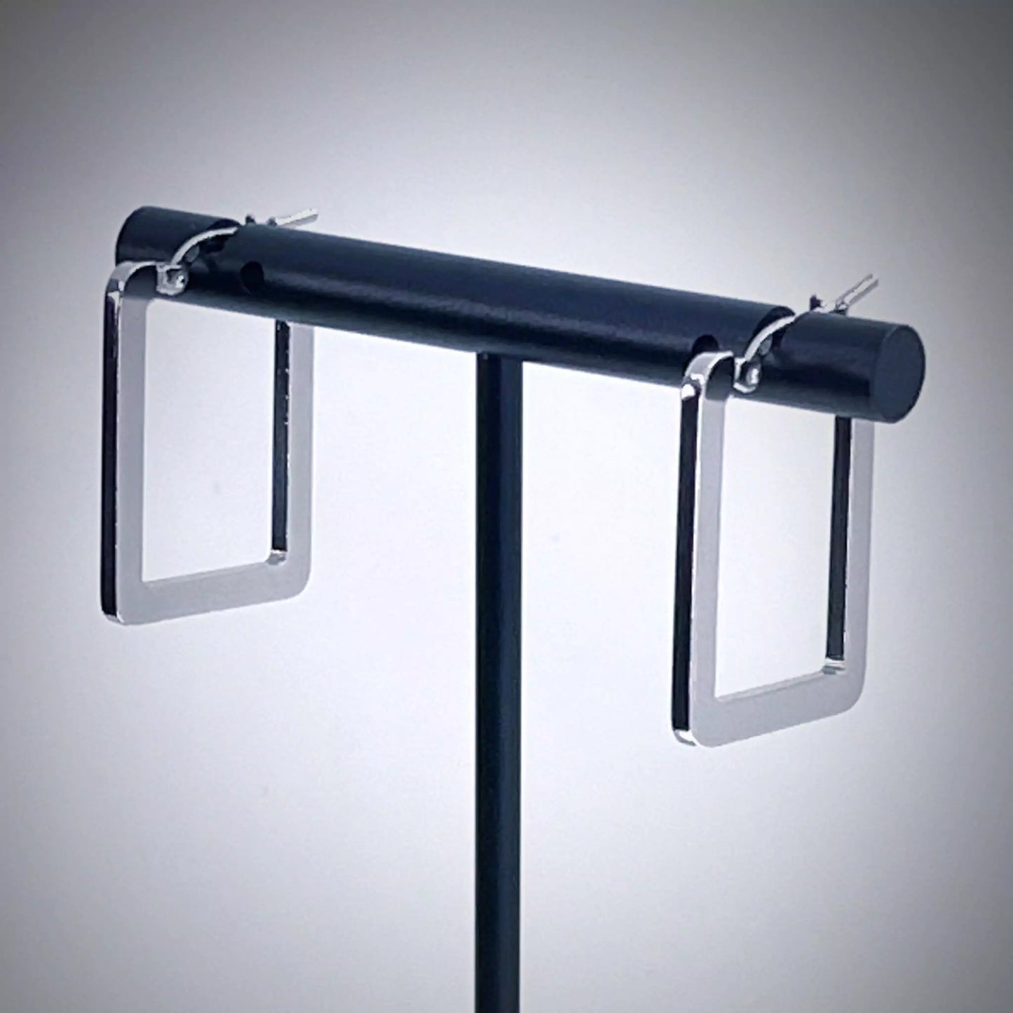 Pair of rectangle silver hoop earrings on earring stand against light gray background