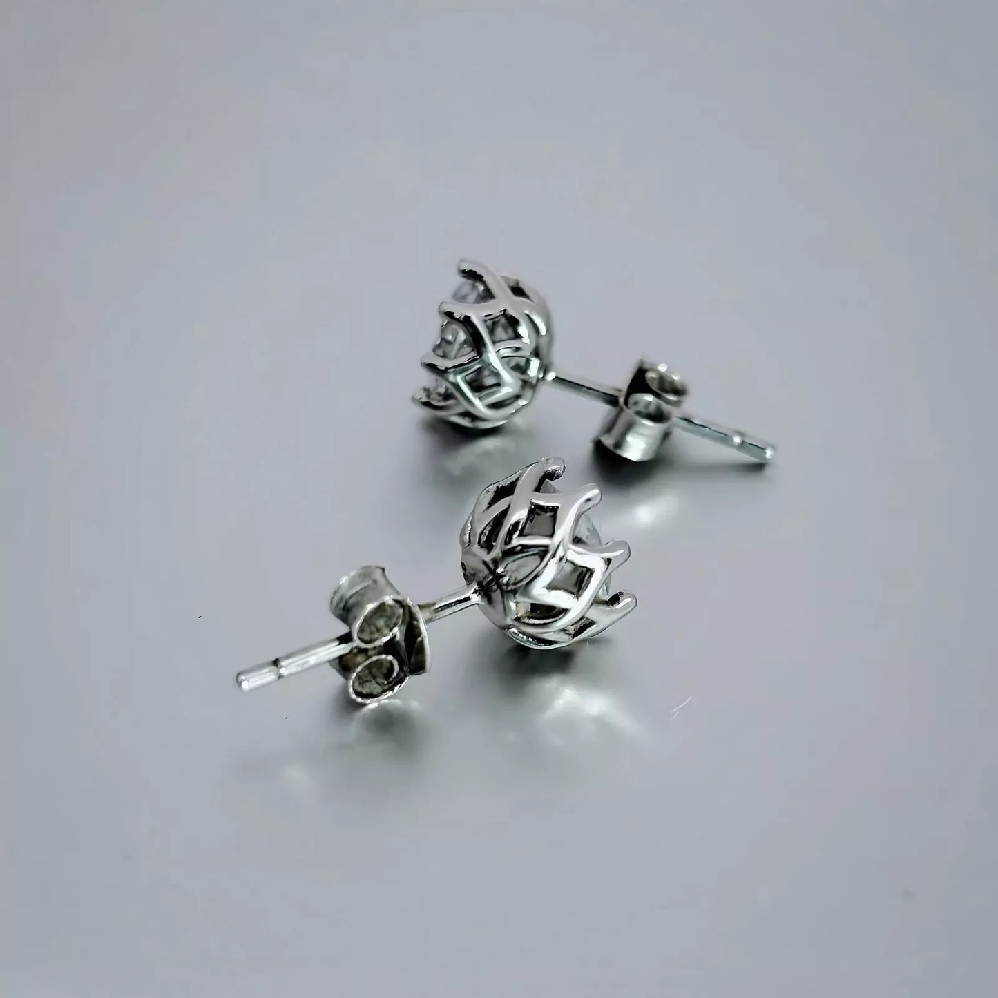 A pair of round stud earrings crafted in Sterling Silver 925,  with clear  Cubic Zirconia placed on a grey background.