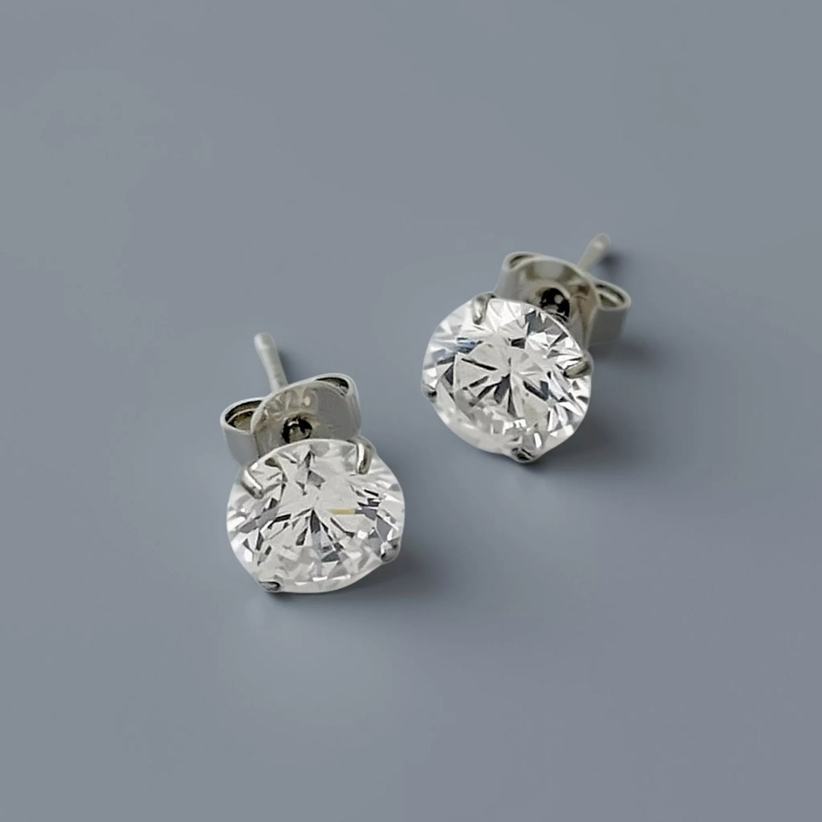 Silver stud earrings crafted in 925 sterling silver featuring clear white round cubic zirconia gemstone displayed on a smooth cool mid grey background with soft diffused lighting.
