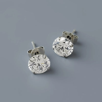Silver stud earrings crafted in 925 sterling silver featuring clear white round cubic zirconia gemstone displayed on a smooth cool mid grey background with soft diffused lighting.
