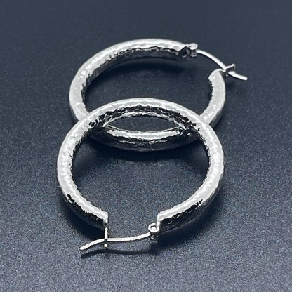 Silver creole hoop earrings crafted in 925 sterling silver on a back background.