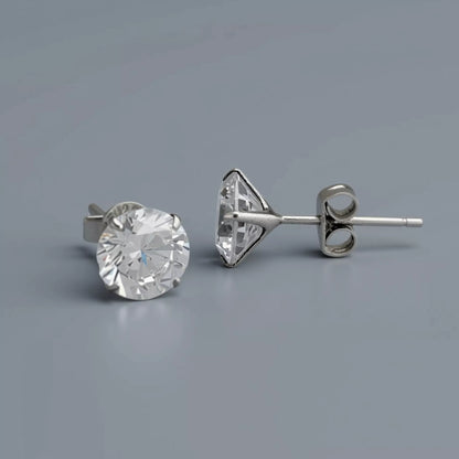A pair of silver stud earrings crafted in 925 sterling silver featuring clear-white round cubic zirconia gemstones, and showing a triangular prong setting with a butterfly back, displayed on a smooth cool mid grey background with soft diffused lighting.