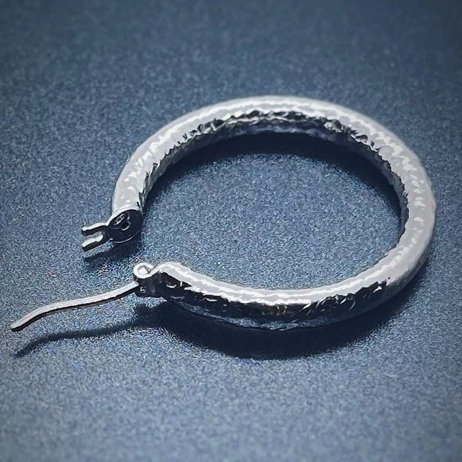 A single silver creole hoop earring crafted in 925 sterling silver on a back background.