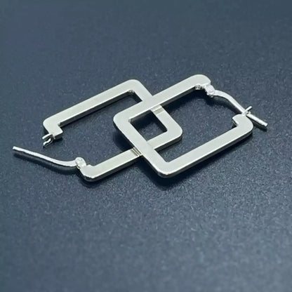 A pair of rectangle silver hoop earrings crafted in 925 sterling silver placed on a dark background.