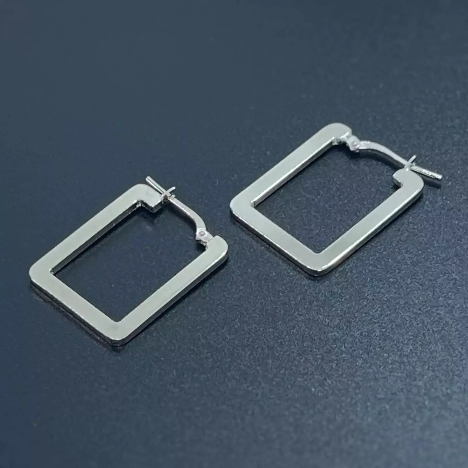 A pair of rectangle silver hoop earrings crafted in 925 sterling silver placed on a dark background.
