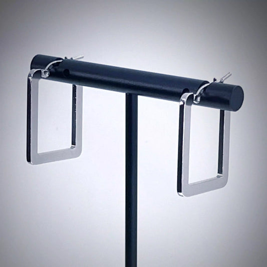 Pair of rectangle silver hoop earrings on earring stand against light gray background